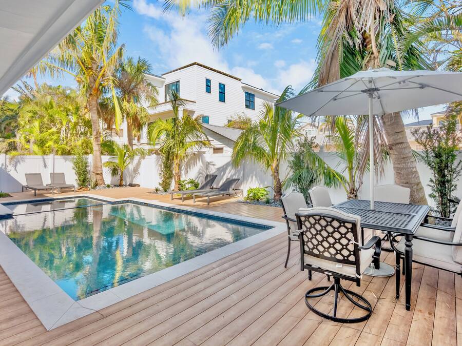 Un área de piscina con terraza de madera, sillas de descanso y una mesa con sillas.
