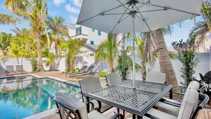 A poolside area with a table and chairs, surrounded by palm trees and a white building. - Captain's Quarters at Anna Maria Island Inn (Bradenton Beach)