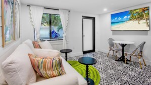 A modern living room with a white sofa, colorful pillows, a small round table, and a large beach-themed painting on the wall. - Captain's Quarters at Anna Maria Island Inn (Bradenton Beach)