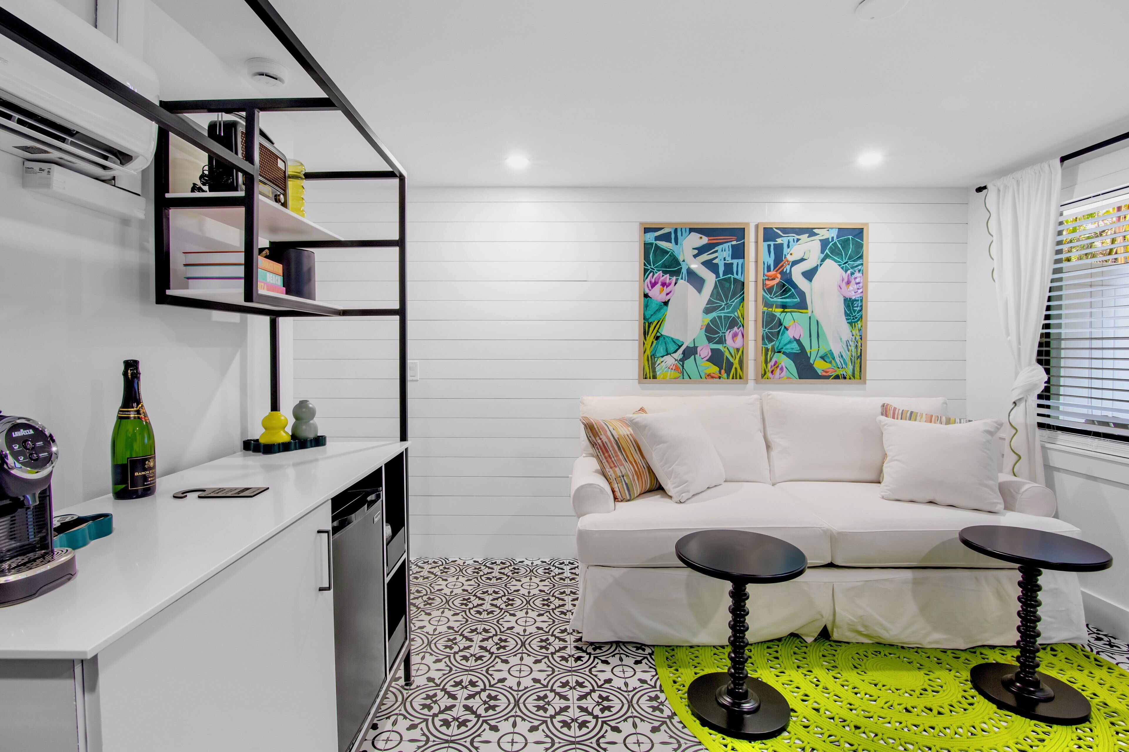 Un soggiorno moderno con un divano bianco, due tavolini neri, un quadro astratto colorato e un pavimento decorato.