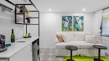 A modern living room with a white sofa, two black side tables, a colorful abstract painting, and a patterned floor.
