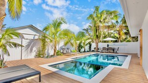 A modern outdoor pool area with wooden decking, lounge chairs, and a dining set. - Captain's Quarters at Anna Maria Island Inn (Bradenton Beach)