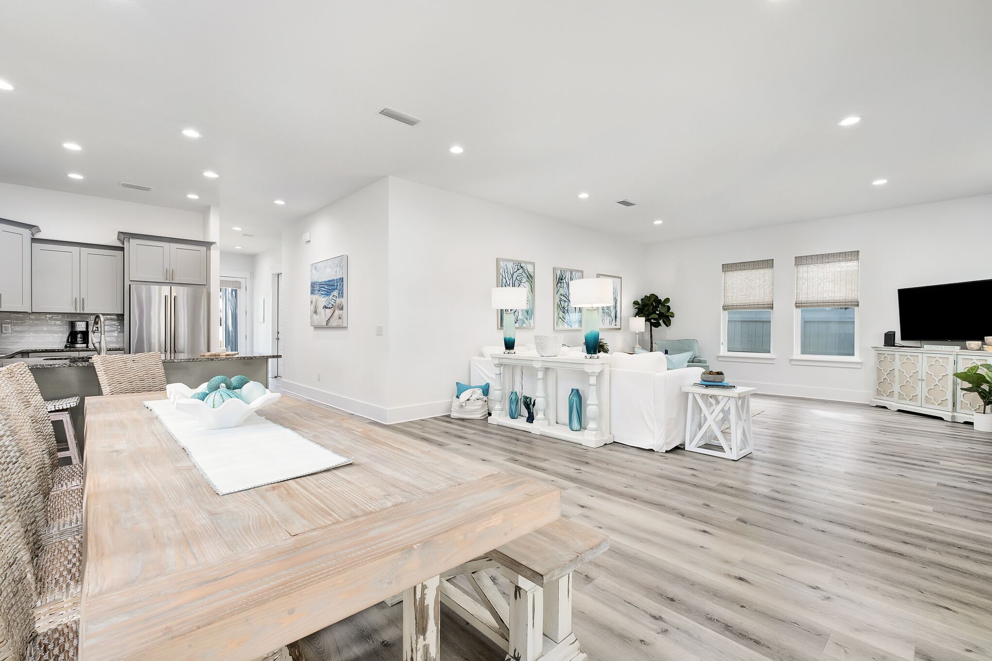 A spacious living area with a wooden dining table, white sofas, and a kitchen in the background.