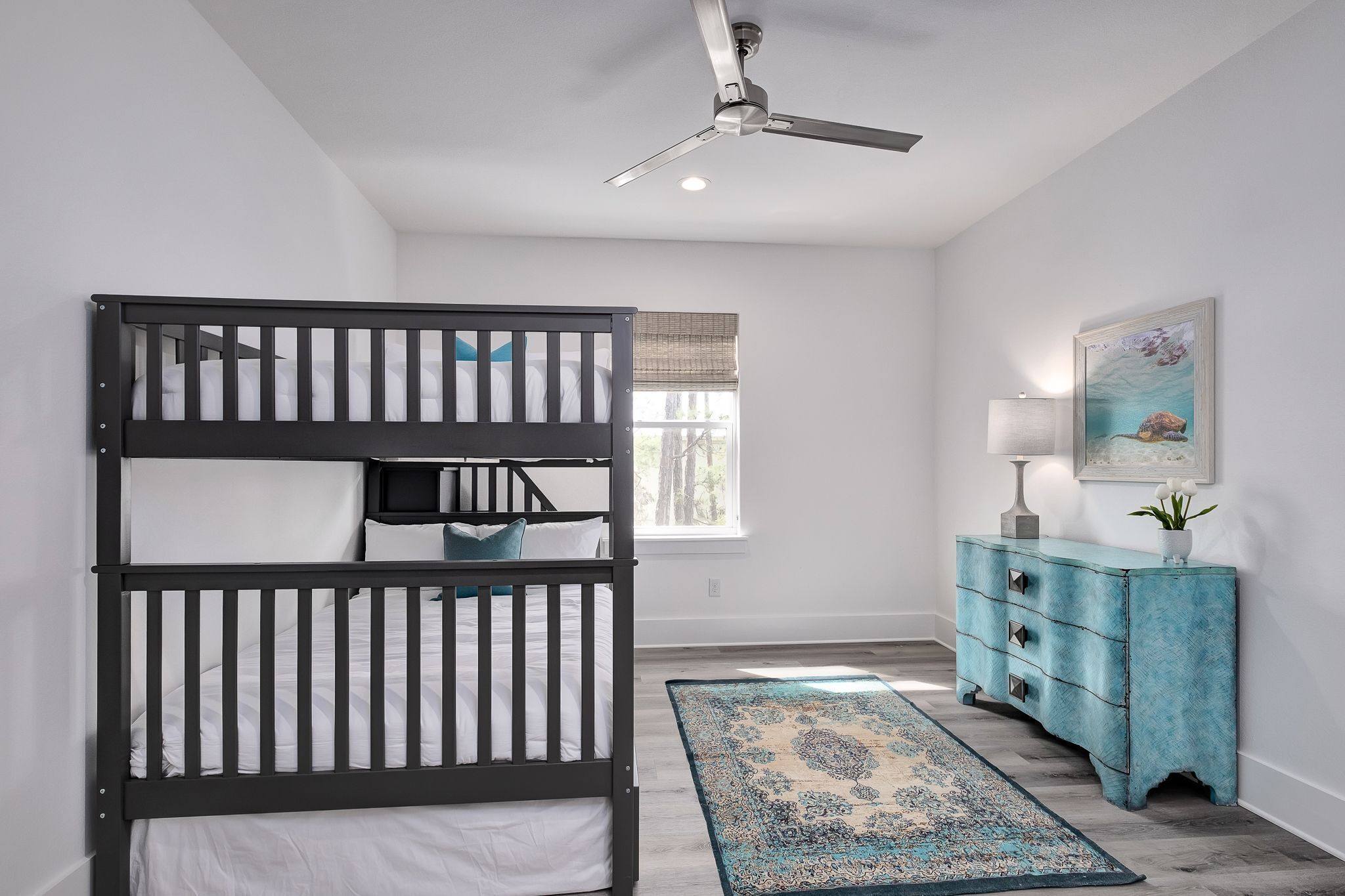 A room with a bunk bed, a ceiling fan, a dresser, and a window with blinds.