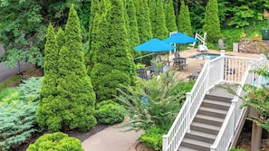 A residential outdoor area with a staircase leading to a deck, surrounded by lush greenery and a swimming pool. - MountainLoft™ - 1 Bedroom Deluxe Villa (Gatlinburg)