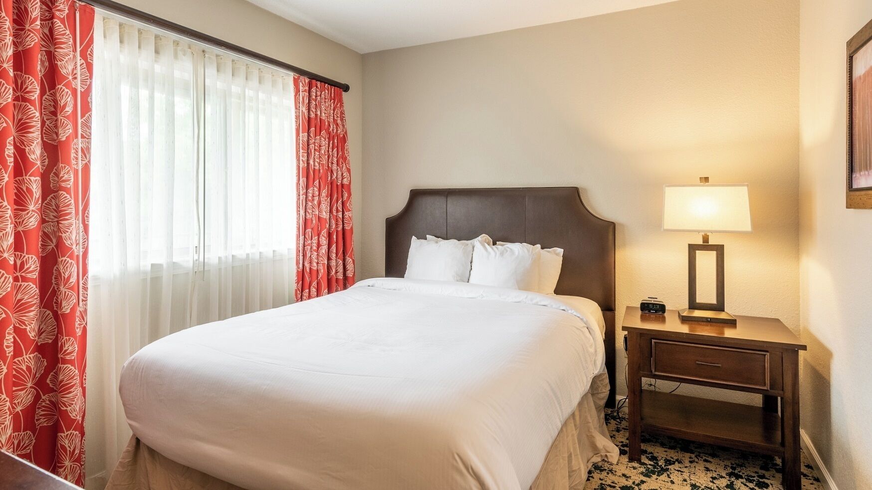 Une chambre d’hôtel avec un lit, une table de chevet avec une lampe et une fenêtre avec des rideaux.