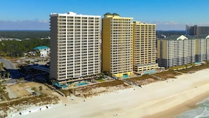 A beachfront hotel with multiple high-rise buildings, a sandy beach, and a clear blue sky. - Ocean Villa 1302 (Panama City Beach)