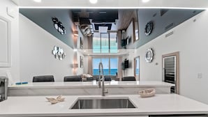 A modern kitchen with a large island, stainless steel appliances, and a view of the ocean through large windows. - Ocean Villa 1302 (Panama City Beach)