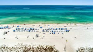 A beach with rows of blue beach chairs and umbrellas, a lifeguard tower, and a clear view of the ocean. - Ocean Villa 1302 (Panama City Beach)