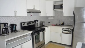 A modern kitchen with white cabinets, stainless steel appliances including a refrigerator, stove, and microwave, and a coffee maker. - Sunset Arms 3: 2brm/2wsr, Airport-Beach-Hipstrip (Montego Bay)