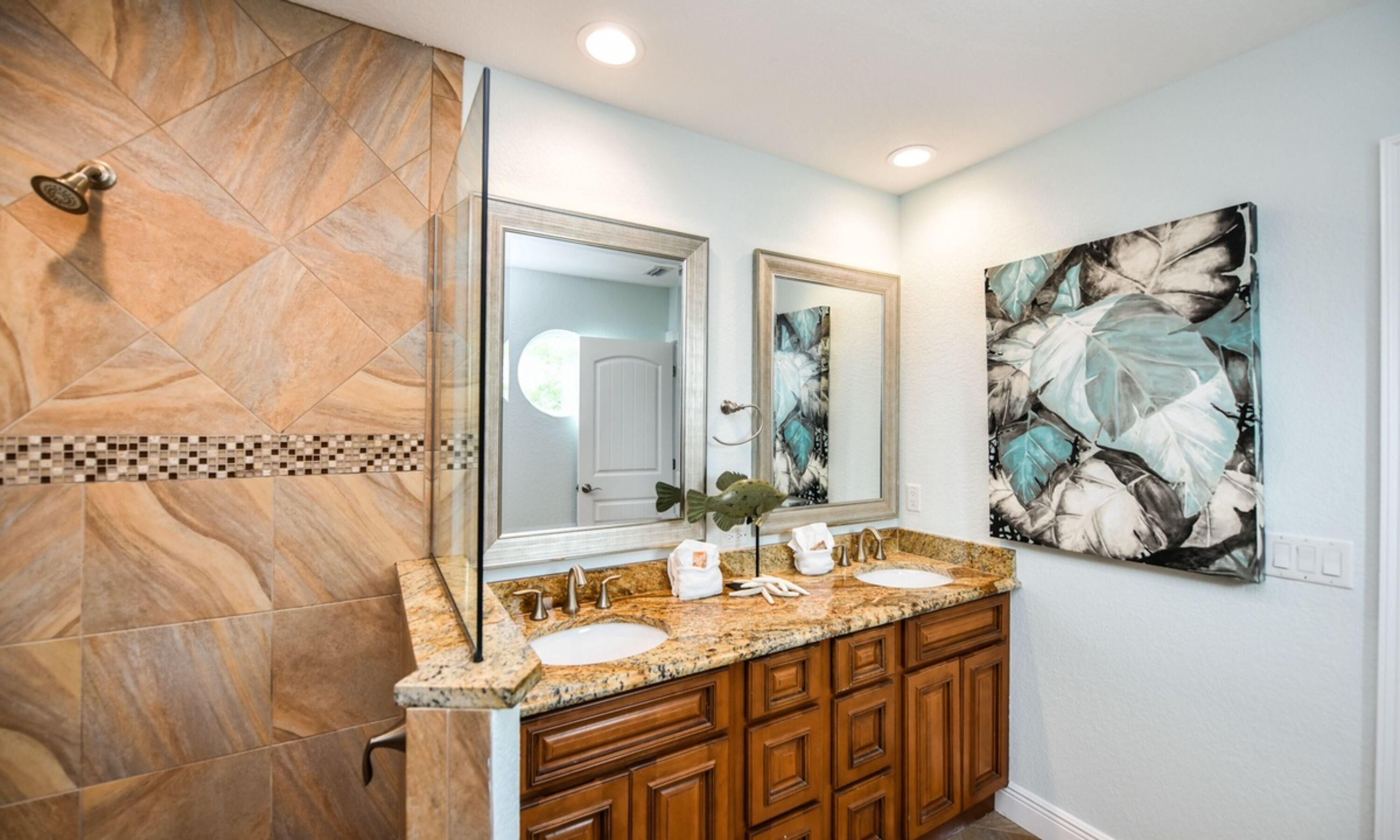 A bathroom with a double sink vanity, a large mirror, and a shower area with a geometric tile design.