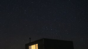 Un petit bâtiment de forme cubique, doté de grandes fenêtres, situé dans un désert, de nuit, sous un ciel étoilé.