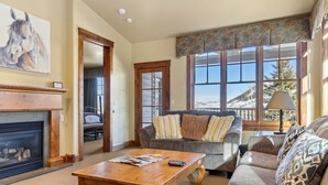 A cozy living room with a fireplace, a sofa, a coffee table, and a large window with a mountain view. - Outpost: Grand View 3140 - Air conditioning! (Jackson)