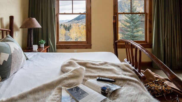 A bedroom with a large window, a bed with a fur throw, a lamp, and a remote control on the bed. - Outpost: Grand View 3140 - Air conditioning! (Jackson)