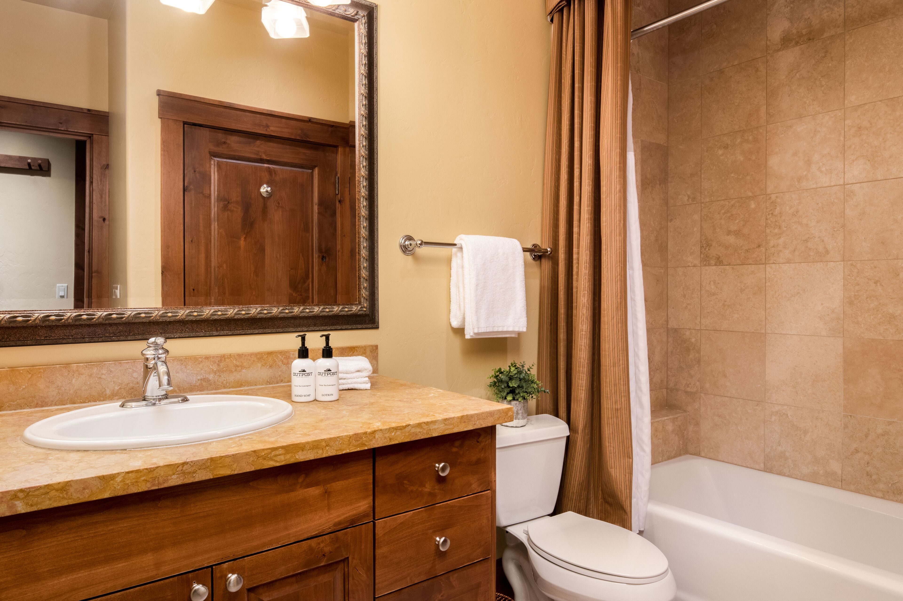 A bathroom with a wooden vanity, a white sink, a mirror, a toilet, and a bathtub.