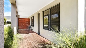 A modern outdoor patio with a wooden deck, a table with chairs, and a wooden fence.