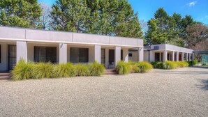 A modern building with a covered outdoor area, gravel ground, and green shrubs.