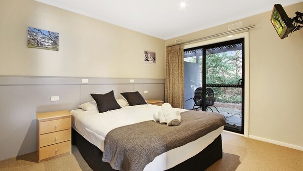 A bedroom with a bed, a nightstand, a chair, and a view through a glass door.