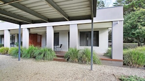 A modern building with a covered patio area, featuring a seating arrangement and a gravel ground. - Grevillea Gardens Unit 8 (BRIGHT)