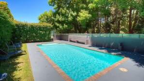 A rectangular swimming pool with a tiled edge, surrounded by a grassy area and a low stone wall.