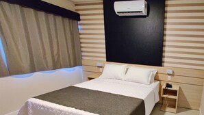 Ein Hotelzimmer mit Bett, Nachttischen, einer Klimaanlage und einem mit Vorhängen versehenen Fenster.
