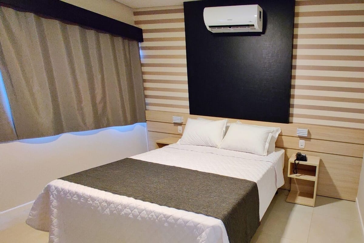 Une chambre d’hôtel équipée d’un lit, de tables de chevet, d’un appareil de climatisation et d’une fenêtre avec des rideaux.