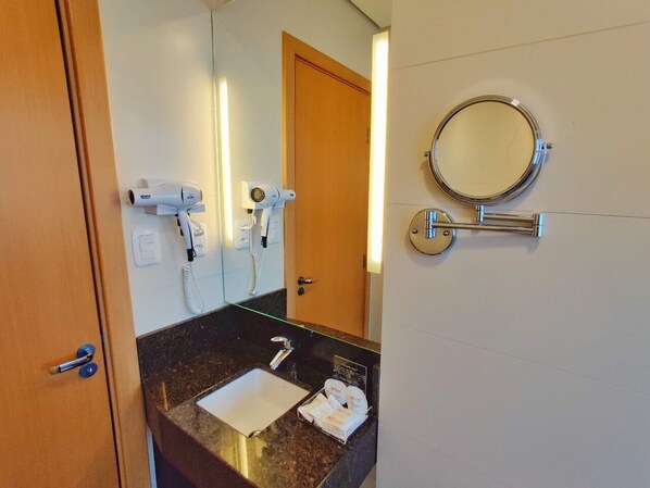 Une salle de bain d’hôtel équipée d’un lavabo, d’un miroir et d’un sèche-cheveux.