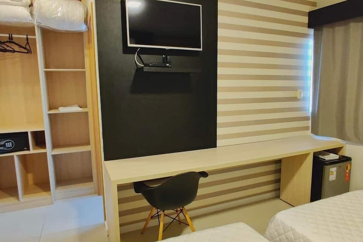 Une chambre d’hôtel comprenant un lit, un bureau avec une chaise, un téléviseur fixé au mur et une armoire avec des vêtements suspendus.