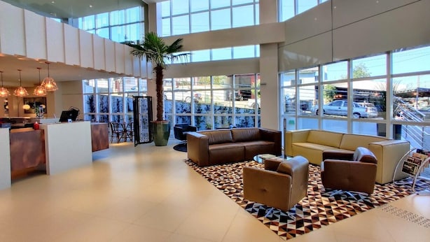 Eine großzügige Lobby mit einer Rezeption, einer Sitzecke und großen Fenstern mit Blick auf den Parkplatz.
