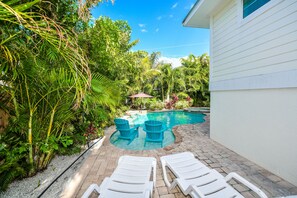 A backyard with a swimming pool, two blue Adirondack chairs, and a white house. - Beach Time AMI by AMI Locals (Holmes Beach)