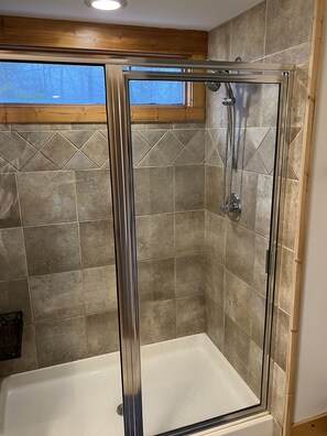 Una ducha con cerramiento de vidrio, una bañera, paredes de azulejos y techo de madera.
