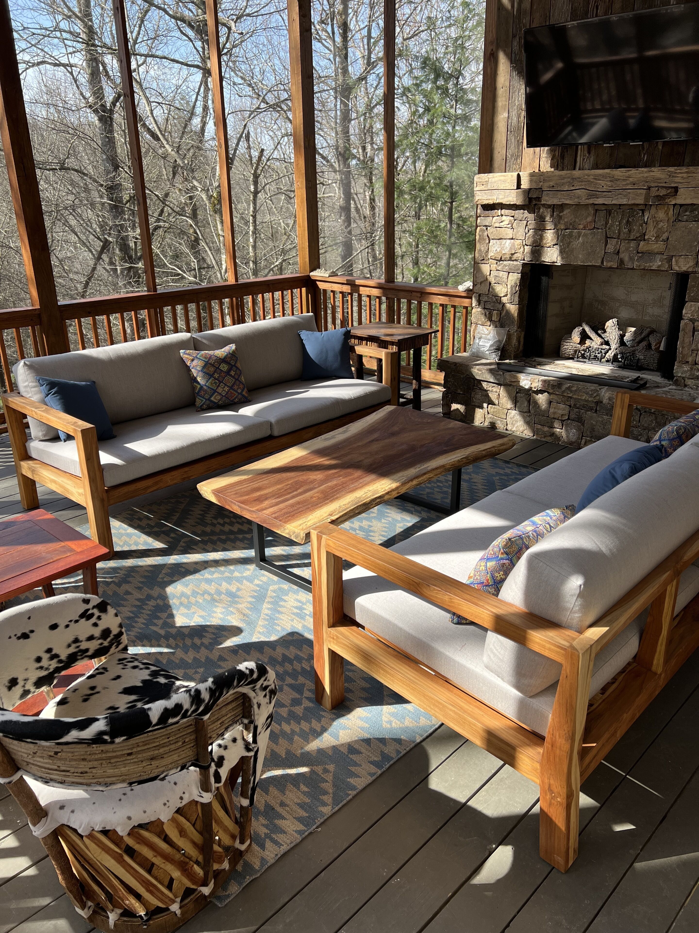 Eine Holzterrasse mit Kamin aus Stein, einer Couch und einem Hundebett.
