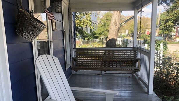 Une véranda avec des fauteuils Adirondack et une table, un panneau de signalisation en arrière-plan et une vue sur une rue résidentielle.