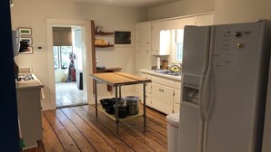 Une cuisine avec un plancher en bois, des armoires blanches, un évier en acier inoxydable et un réfrigérateur blanc.