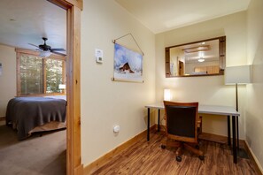 Une pièce comprenant un lit, un bureau, une chaise, un ventilateur de plafond, une fenêtre avec des stores et un miroir fixé au mur.