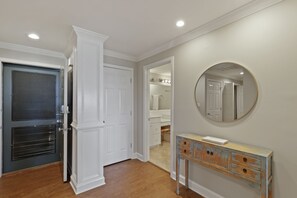 Een hal met een houten vloer, een witte deur, een spiegel en een dressoir met lades.