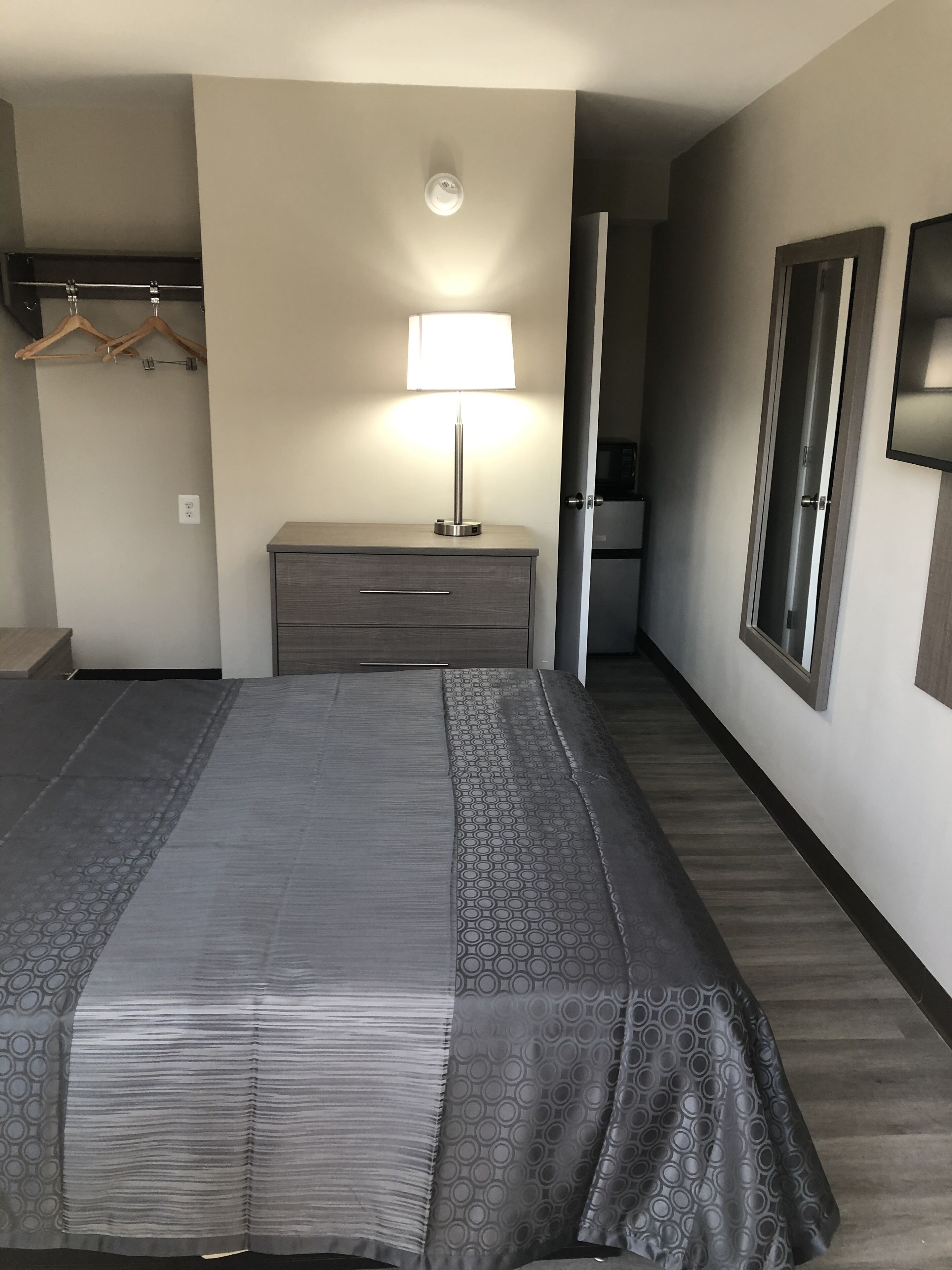A hotel room with a large bed, a bedside table with a lamp, a wardrobe, and a mirror on the wall.
