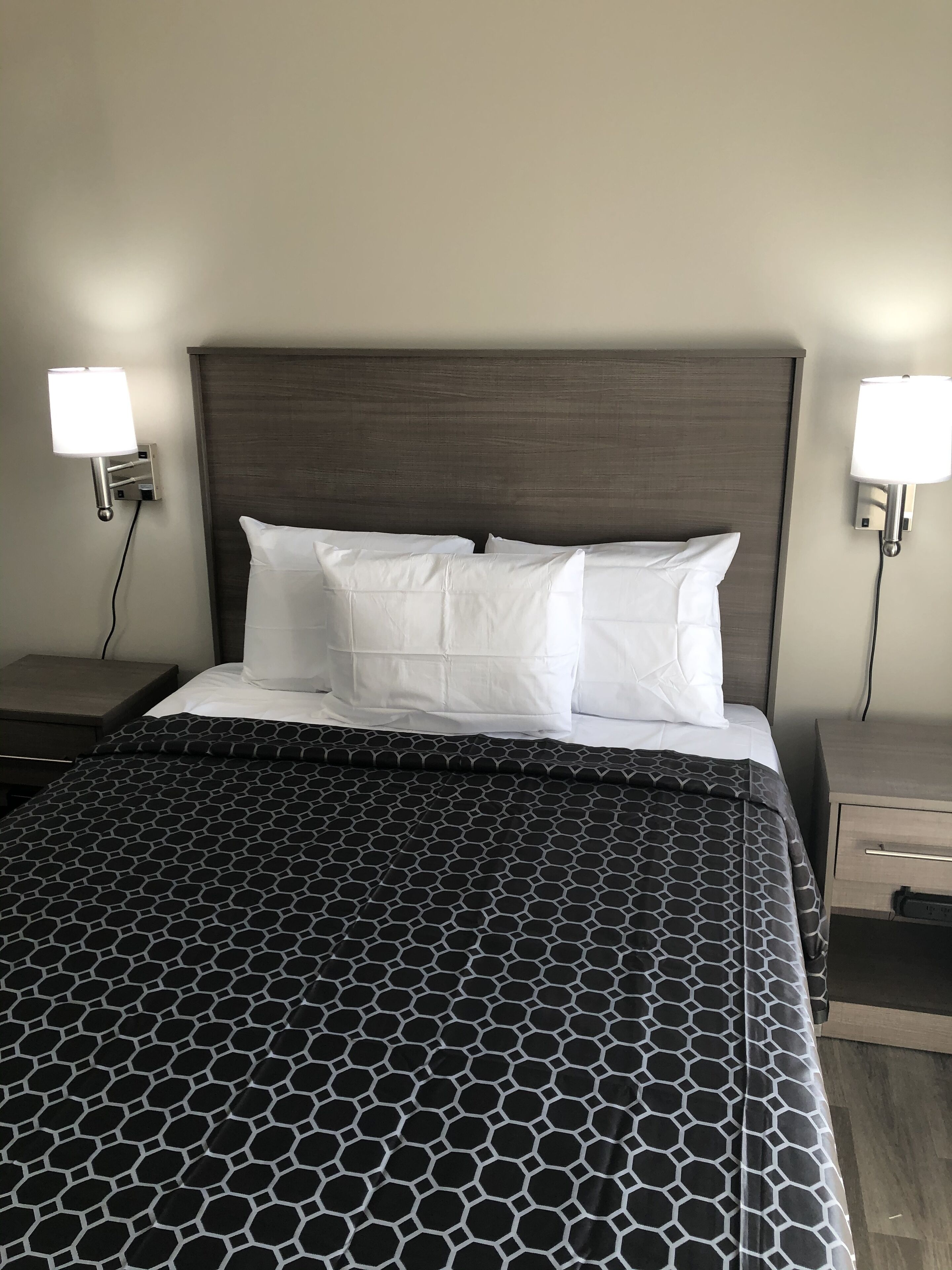Cama bem arrumada com colcha de padrão geométrico, duas almofadas brancas e cabeceira de madeira escura.