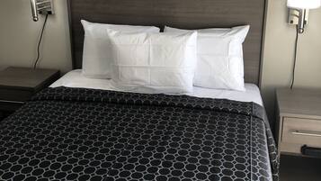 Cama bem arrumada com colcha de padrão geométrico, duas almofadas brancas e cabeceira de madeira escura.