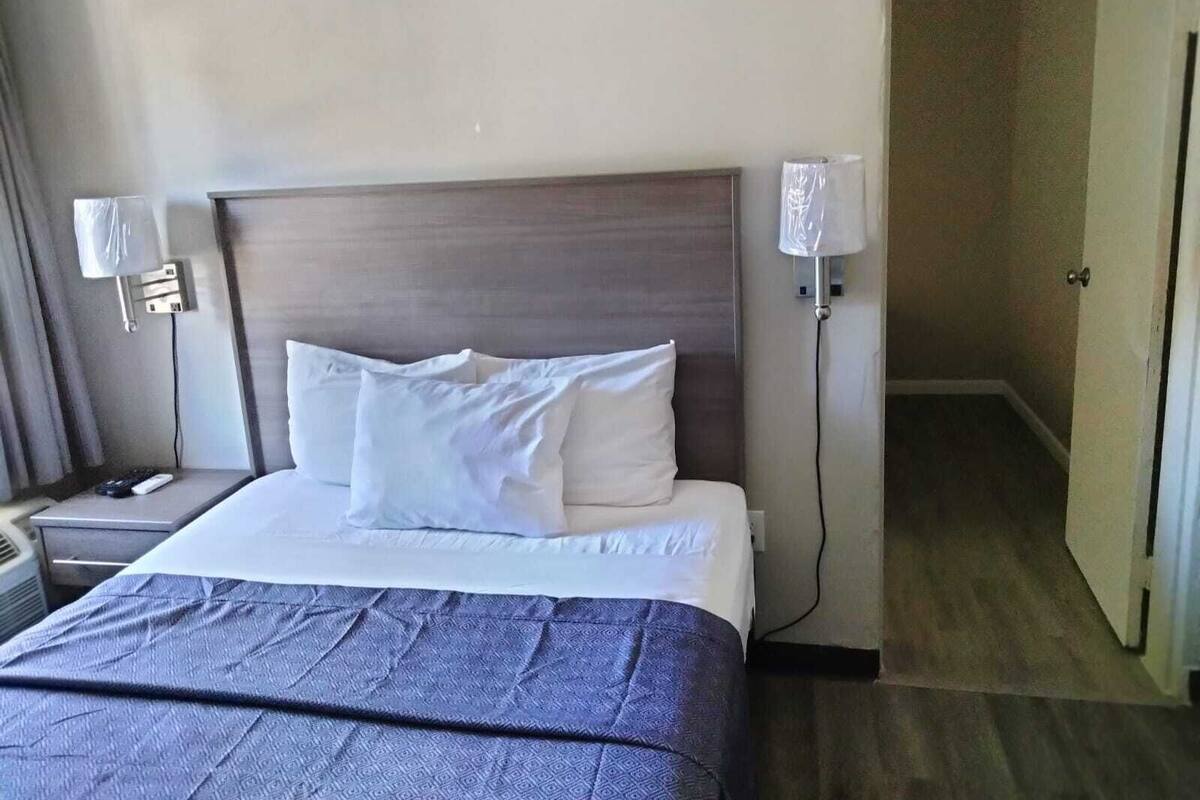 A hotel room with a large bed, two bedside lamps, a nightstand, and a door leading to another room.