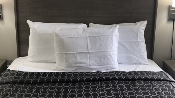 A bed with a dark headboard, white pillows, and a black and white patterned bedspread. - Trolley Stop Motel (Media)