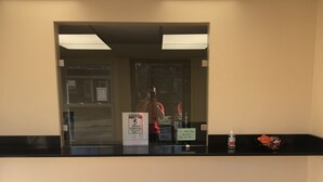 A reception area with a wooden floor, a black reception desk, a trash can, and a sign indicating a COVID-19 safety measure. - Trolley Stop Motel (Media)