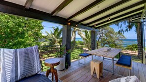 Una terraza al aire libre con una mesa y sillas de madera, rodeada de abundante vegetación y vistas al océano.