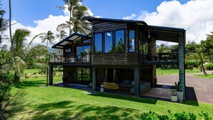Una casa moderna de dos pisos con ventanas grandes, un balcón y una silla colgante.