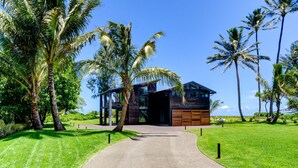 Una casa moderna con entrada de concreto, rodeada de palmeras y un césped cuidado.