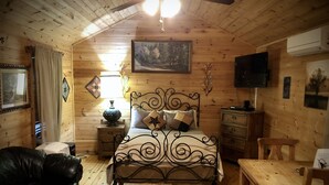 A cozy wooden cabin bedroom with a bed, a wooden dresser, a black leather couch, and a dining table. - Cabin in the Country (Fredericksburg)