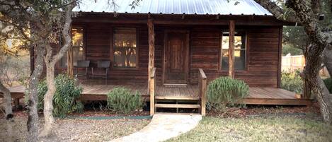 A rustic wooden cabin with a porch, two windows, and a metal roof.