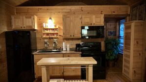 A wooden cabin kitchen with a refrigerator, stove, microwave, and wooden cabinets. - Cabin in the Country (Fredericksburg)