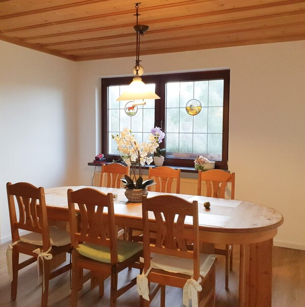 Un coin repas avec une table et des chaises en bois, un lustre et une fenêtre ornée de vitraux.