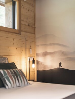 A room with wooden walls, a bed with pillows, a wall-mounted light, and a mural of a person on a hill. - Veliski-Lodge, a chalet for rent in Haute-Maurienne (Modane)